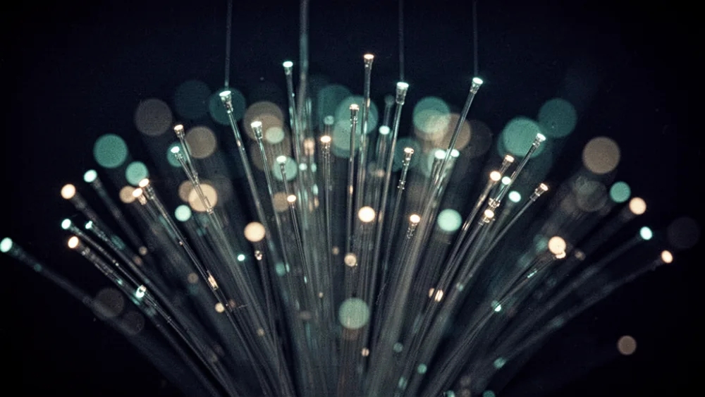 Fine fibre-optic strands fanning outward and glowing teal and white against a dark background